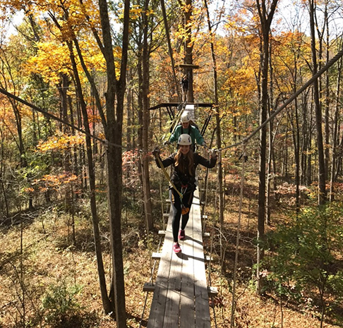 women crossing zipline bridge in fall foliage