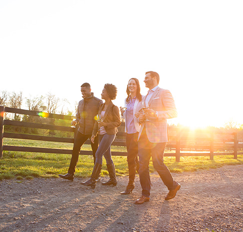 Four people walking along a fence with wine glasses in hand