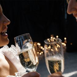 Two guests toast with glasses of champagne beside glowing holiday lights.