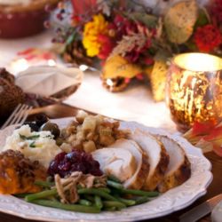 Thanksgiving plate with sliced turkey, stuffing, green beans and cranberry sauce, set beside a candle and autumn centerpiece.