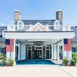 The front entrance of Salamander Middleburg with white columns and two American flags displayed on either side, welcoming guests beneath the covered portico on a bright summer day.
