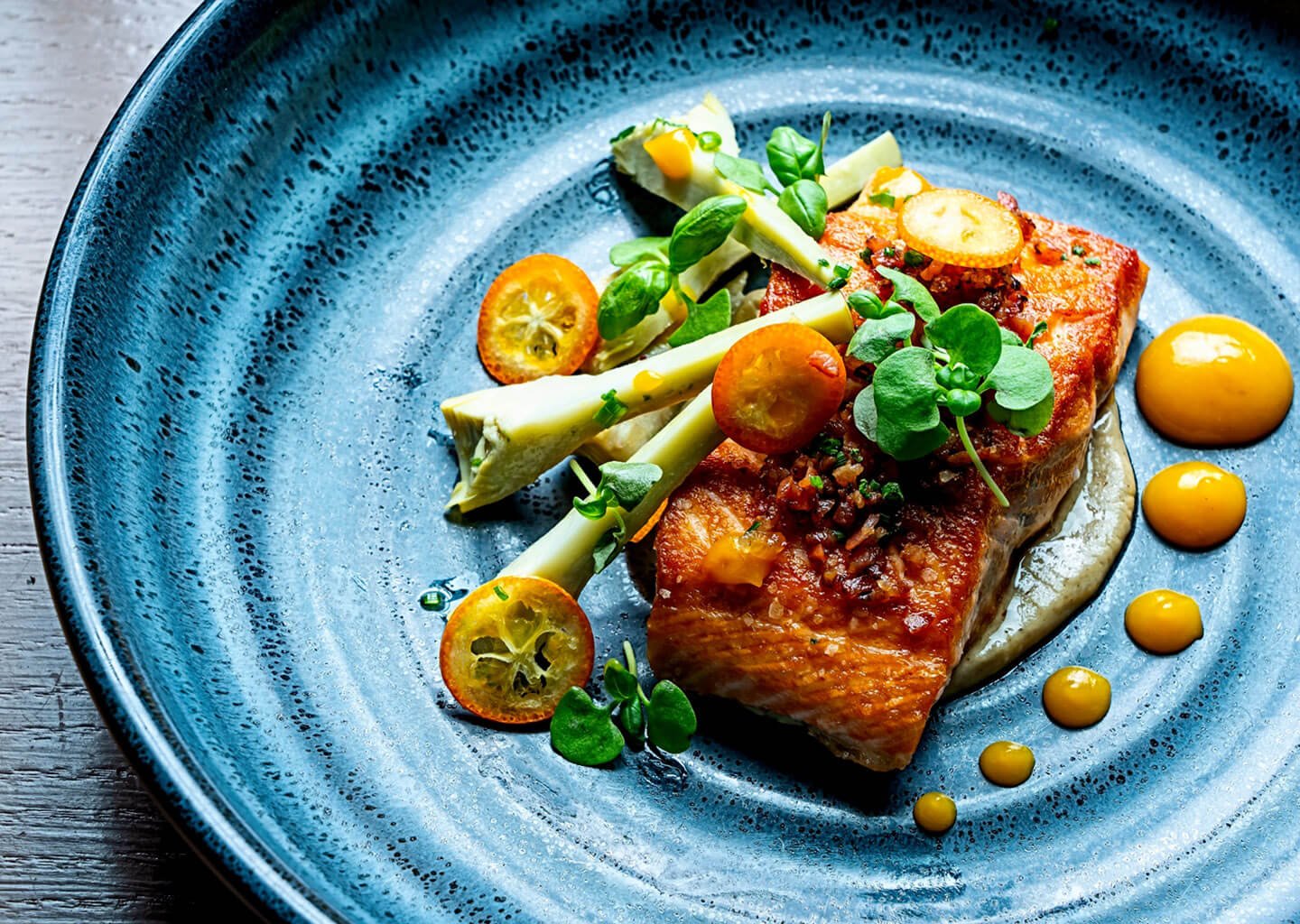 Fish with kumquats, yellow sauce dots, and a microgreen garnish