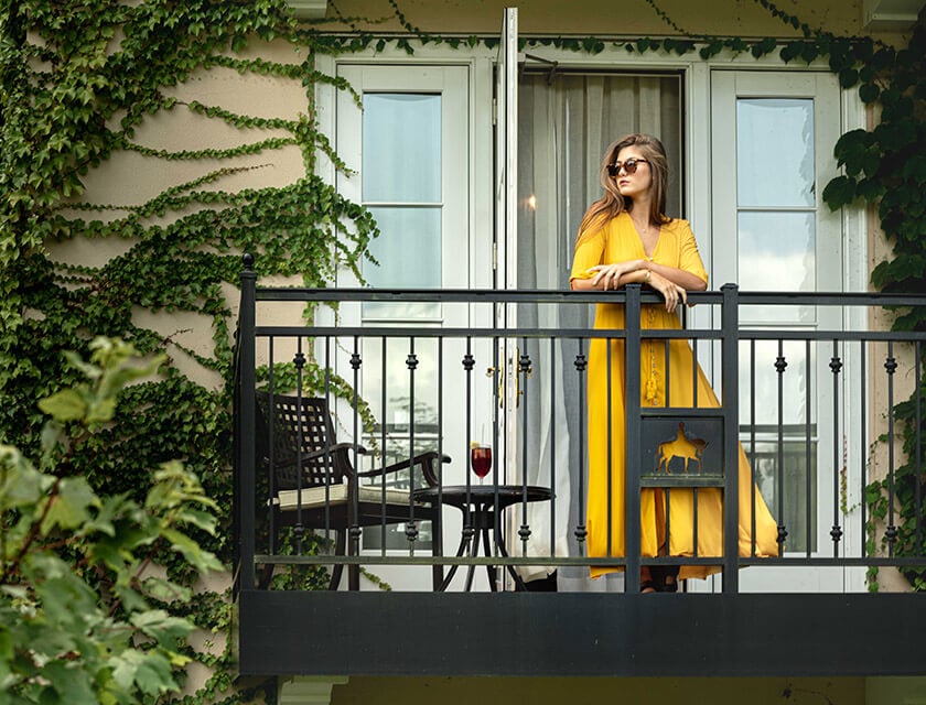 Woman relaxing on balcony railing in a yellow dress and sunglasses